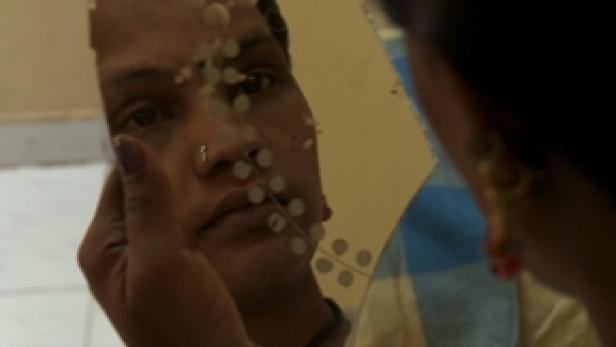 Eine Person mit Nasenring betrachtet sich in einem Spiegel.