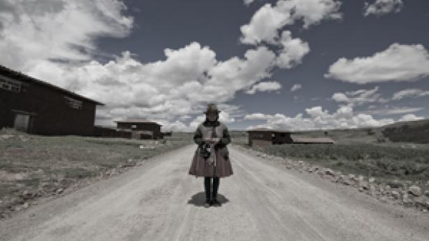 Eine Frau in traditioneller Kleidung steht auf einer Landstraße vor einer ländlichen Szenerie.