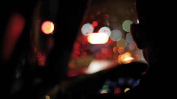 Eine Person fährt nachts Auto, mit verschwommenen Lichtern im Hintergrund.