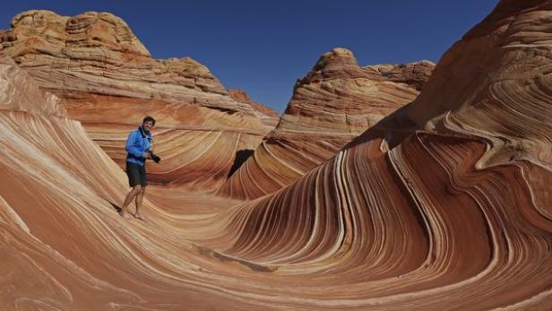Ein Mann steht barfuß in der wellenförmigen Felsformation „The Wave“ in Arizona.