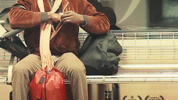 Ein Mann sitzt auf einer Bank mit einer roten Tasche, Plakat für den Film „When Paul came over the Sea“.