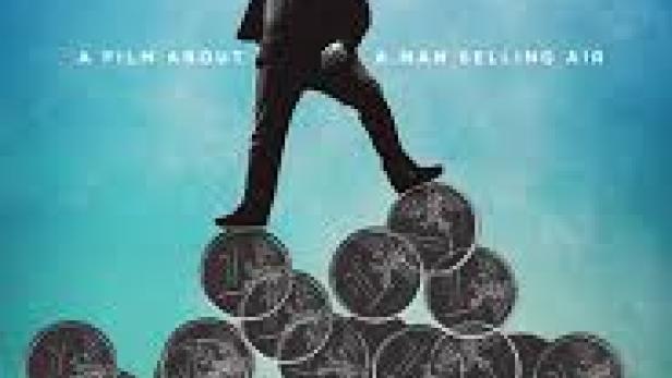 Ein Mann steht auf einem Haufen Münzen vor dem Filmplakat von „Holy Air“.