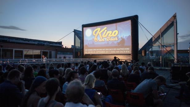 Zuschauer sitzen vor einer Leinwand des „Kino am Dach“ Open-Air-Kinos.