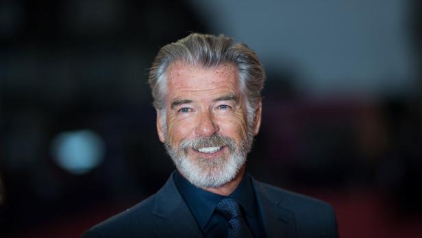 Porträt von Pierce Brosnan mit grauem Haar und Bart in einem dunklen Anzug.