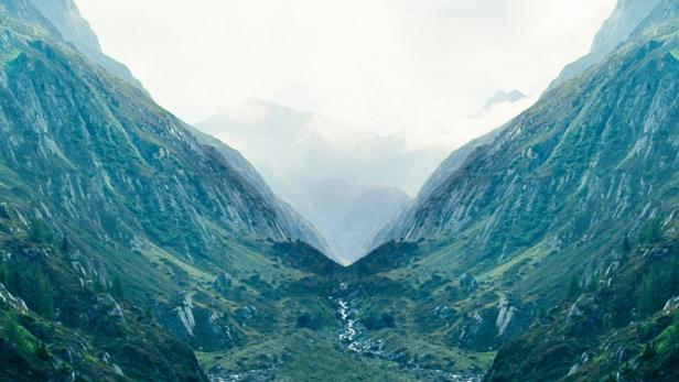 Ein Mann steht in einem Tal und blickt auf einen Gebirgsbach.