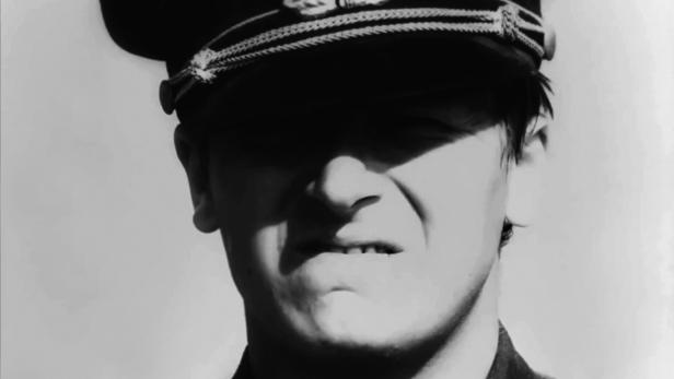 Ein Mann mit Uniformmütze, dessen Gesicht im Schatten liegt.