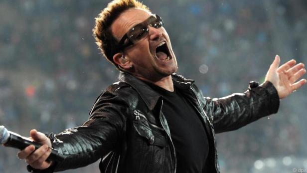 Bono, Sänger der Band U2, singt mit Sonnenbrille und Lederjacke auf der Bühne.