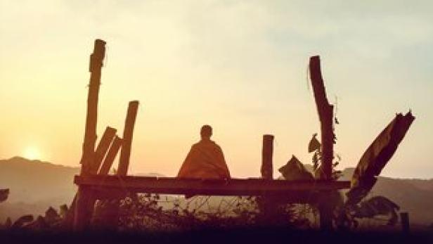 Das Filmplakat für „Weltreise mit Buddha“ zeigt einen Mönch vor einer Landschaft im Sonnenuntergang.