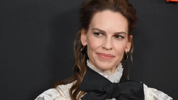 Hilary Swank mit einem weißen Spitzenoberteil und einer schwarzen Schleife.