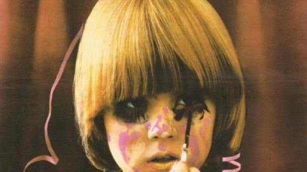 Ein Mädchen mit Farbe im Gesicht schminkt sich vor einem Vorhang.