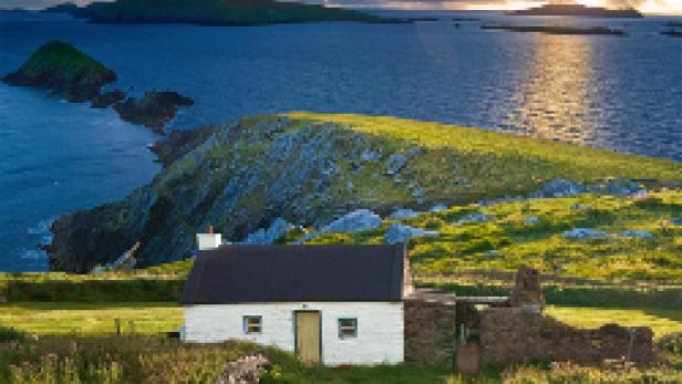 Ein kleines, weißes Haus auf einer grünen Insel vor der Küste Irlands.