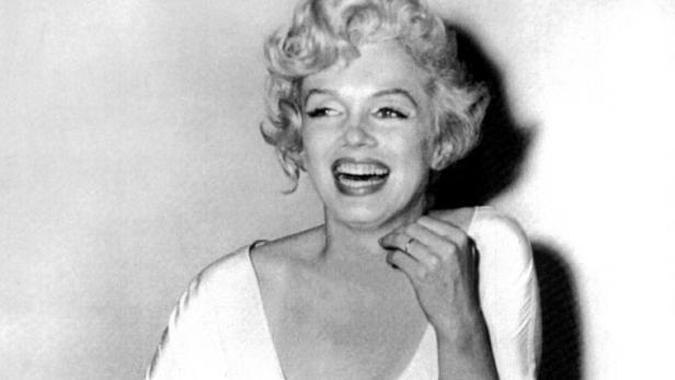 Marilyn Monroe sitzt lachend in einem Sessel.