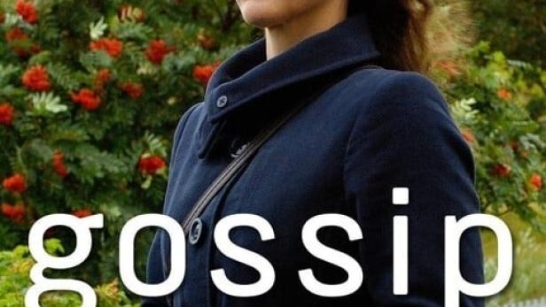 Eine Frau in einem Mantel steht vor einem Strauch mit roten Beeren.