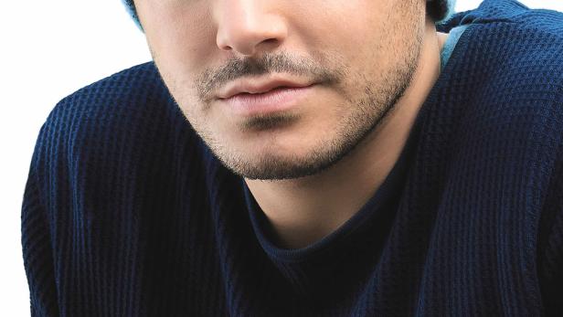 Ein Mann mit hellblauer Mütze und blauem Pullover blickt in die Kamera.