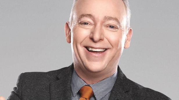 Ein lächelnder Mann im Anzug vor dem Schriftzug „Le tricheur“.