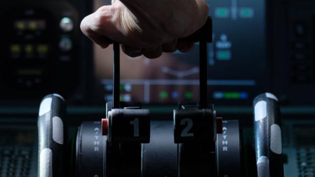 Die Hand eines Piloten bedient die Schubhebel im Cockpit eines Flugzeugs.
