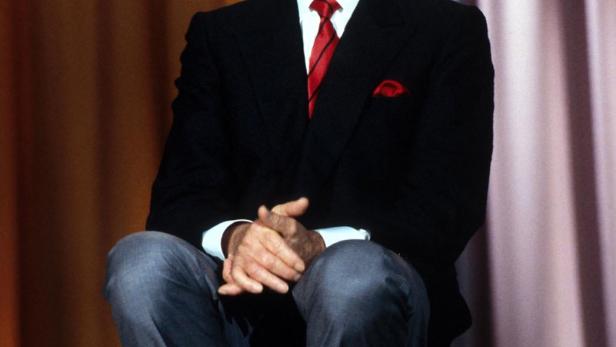 Johnny Carson sitzt auf einem Stuhl vor einem Vorhang.
