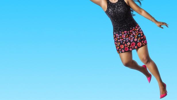 Mindy Kaling schwebt am Himmel mit grünen Ballons, im Hintergrund die Skyline von New York.