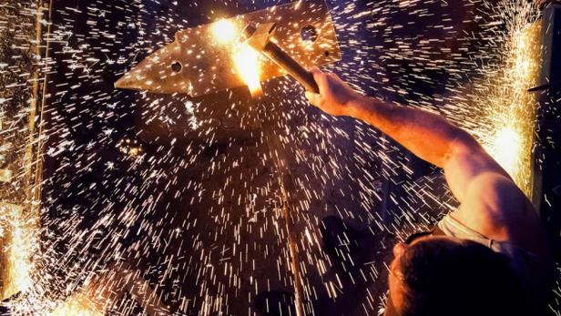 Ein Schmied bearbeitet glühendes Metall mit einem Hammer, Funken sprühen.