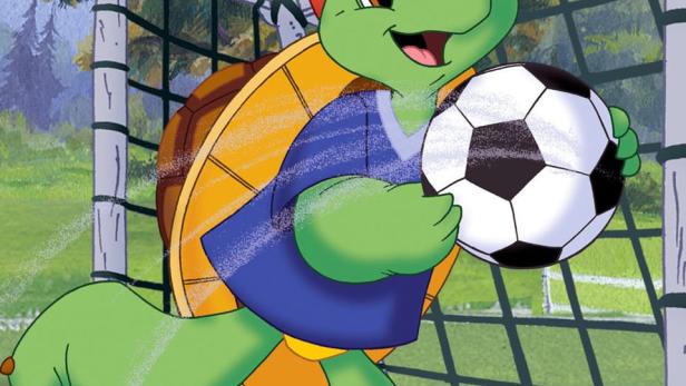 Franklin, die Schildkröte, hält einen Fußball vor einem Fußballtor.