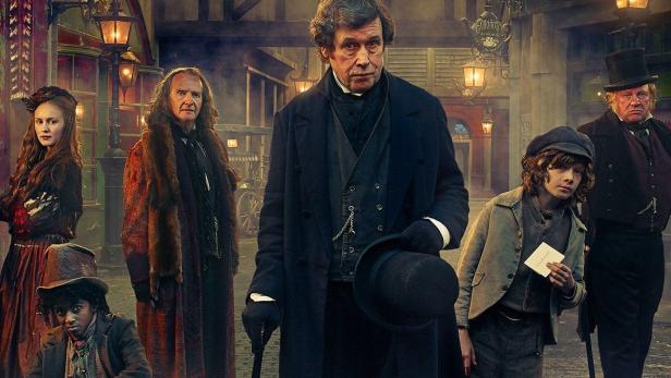 Das Filmplakat für „Dickensian“ zeigt eine Gruppe von Menschen in Kostümen des 19. Jahrhunderts auf einer Kopfsteinpflasterstraße.