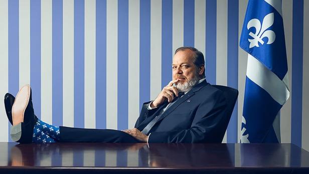 Ein Mann sitzt mit Füßen auf dem Tisch vor der Flagge von Québec; Titel „La Maison-Bleue“.