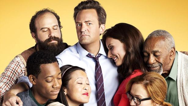 Die Besetzung der Fernsehserie „Go On“ umarmt sich vor einem gelben Hintergrund.