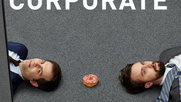 Zwei Büroangestellte liegen auf dem Teppichboden, getrennt durch einen Donut.