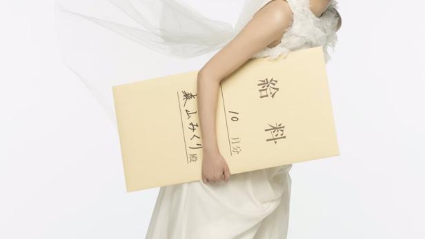 Eine Frau im Brautkleid und Turnschuhen hält einen Umschlag mit der Aufschrift „Gehalt“.
