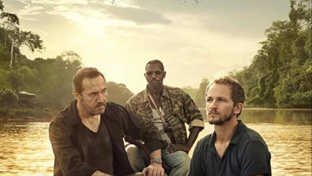 Drei Männer sitzen in einem Boot auf einem Fluss im Filmplakat zu „Guyane“.