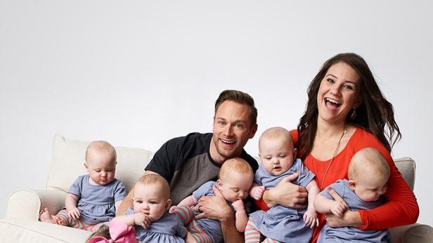 Ein Mann und eine Frau sitzen mit ihren Fünflingen und einer weiteren Tochter auf einem Sofa.