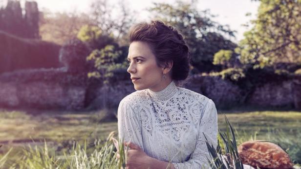Eine Frau im weißen Kleid sitzt im Gras vor dem Hintergrund des Films „Howards End“.