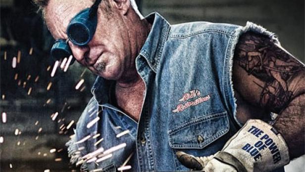 Ein Mann mit Schweißerbrille schweißt Metall in der Werkstatt „American Restoration“.
