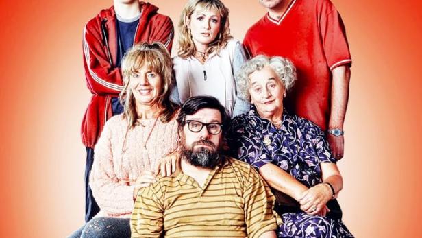 Das Ensemble der britischen Sitcom „The Royle Family“ posiert vor einem roten Hintergrund.