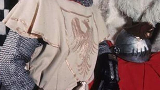 Ein Mann in Ritterrüstung posiert vor einem roten Vorhang.