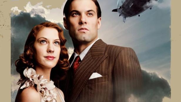 Ein Filmposter für „Hindenburg“ mit einem Paar und einem Luftschiff im Hintergrund.