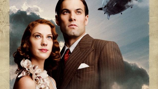 Ein Paar im Stil der 1930er Jahre vor einem Zeppelin am Himmel, möglicherweise eine Filmszene zum Thema „Hindenburg“.