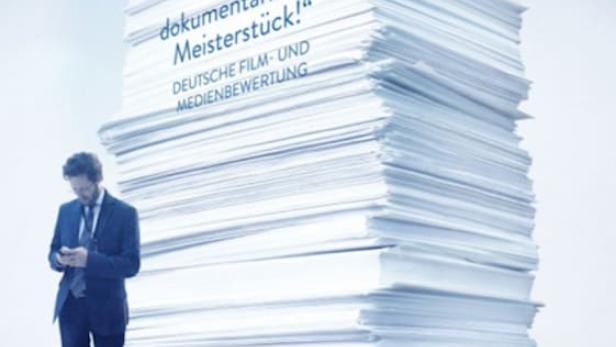Das Filmplakat für „Democracy – Im Rausch der Daten“ zeigt einen Mann vor einem riesigen Papierstapel.