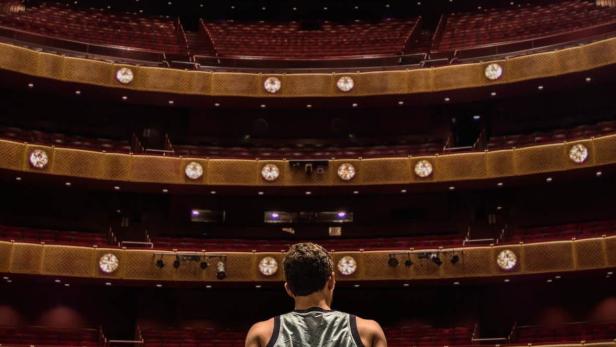 Ein Mann sitzt auf der Bühne und blickt in den leeren Zuschauerraum eines Theaters.