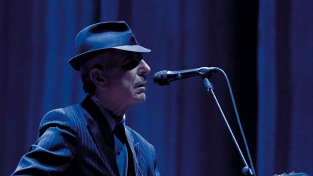 Leonard Cohen tritt live in London mit Gitarre und Hut auf einer Bühne auf.
