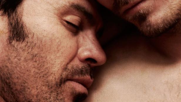 Zwei Männer liegen eng umschlungen, die Augen geschlossen.