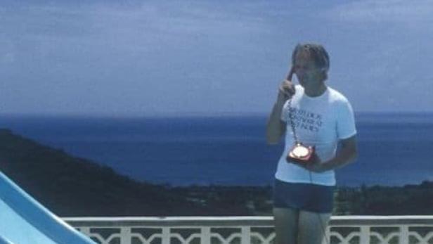 Ein Mann telefoniert mit einem roten Telefon am Pool mit Meerblick.