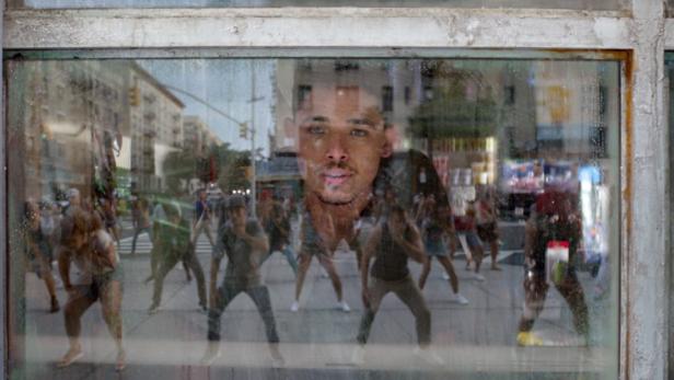 Eine Gruppe von Tänzern spiegelt sich in einem schmutzigen Schaufenster.