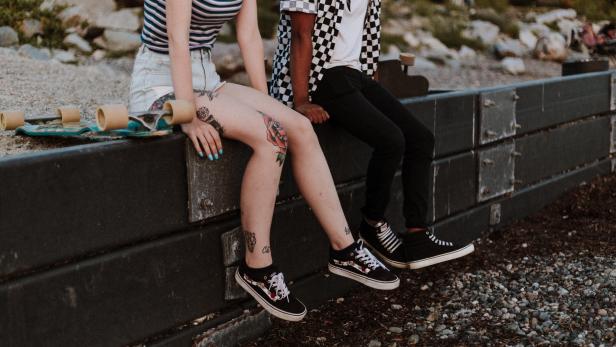 Ein Pärchen sitzt auf einer Wandmauer. Die Frau trägt ein schwarz-weiß gestreiftes und der Mann ein kariertes Shirt. 