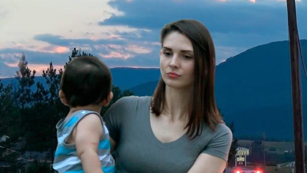 Eine Frau hält ein Kind im Arm, während ein Krankenwagen auf einer Landstraße fährt.