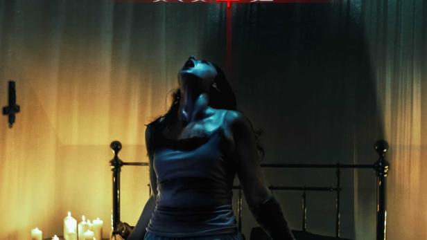 Eine gefesselte Frau kniet auf einem Bett, im Hintergrund das Filmposter für „The Last Rite“.