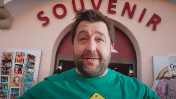 Ein Mann steht vor einem Souvenirladen und trägt ein grünes T-Shirt mit der Aufschrift „No Kangaroos“.