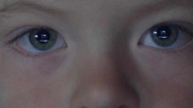 Nahaufnahme des Gesichts eines Kindes mit hellen Haaren und grünen Augen.