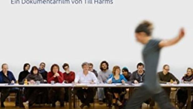 Das Filmplakat für „Die Prüfung“ zeigt eine Gruppe von Menschen an einem Tisch und eine Person, die springt.