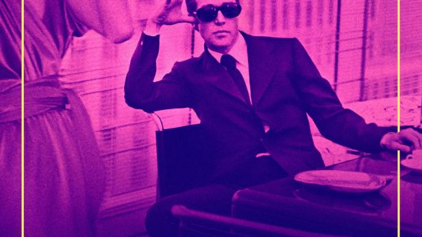 Ein Mann mit Sonnenbrille sitzt an einem Schreibtisch, im Vordergrund der Titel „Halston“.